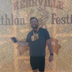 Man wearing medal standing in front of Kerrvile Tri sign
